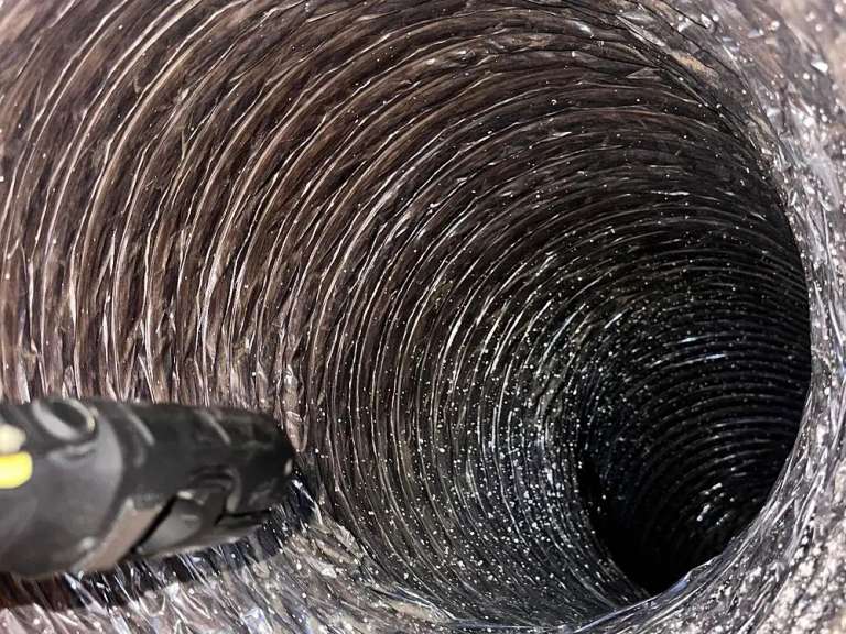 El interior acanalado de aluminio de un ducto de aire flexible después de la limpieza, con la punta de una manguera de aspiración abajo a la izquierda