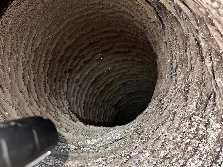El interior acanalado de un ducto de aire flexible cubierto de polvo, con la punta de una manguera de aspiración abajo a la izquierda