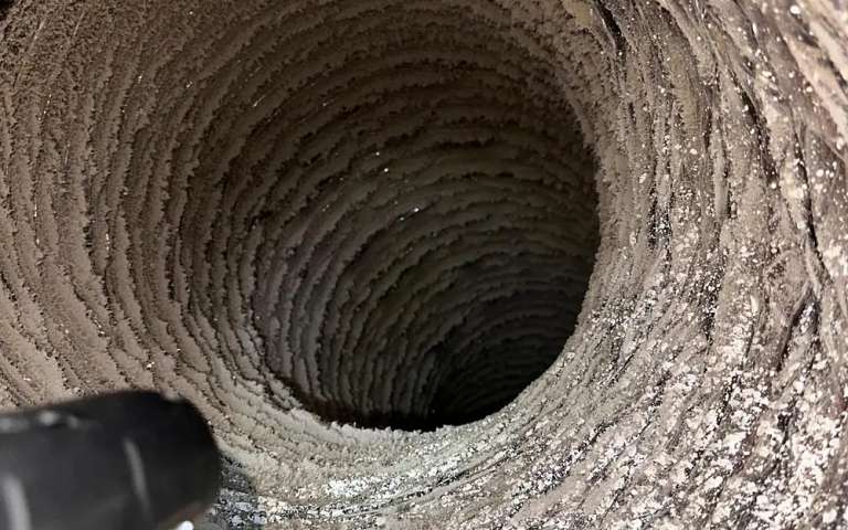 El interior acanalado de un ducto de aire flexible cubierto de polvo, con la punta de una manguera de aspiración abajo a la izquierda