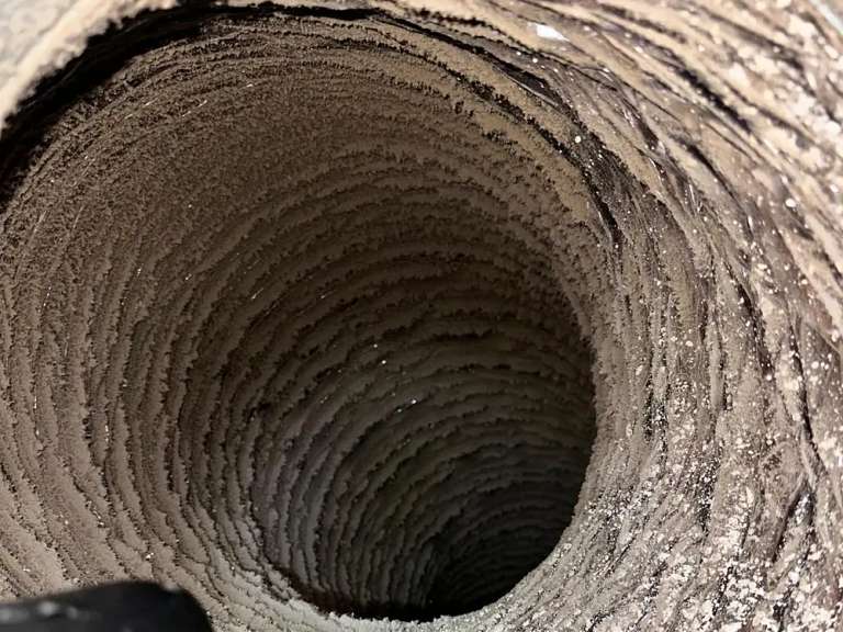 Vista hacia el fondo de un ducto flexible con la pared interior acanalada cubierta de polvo y pelusa gris