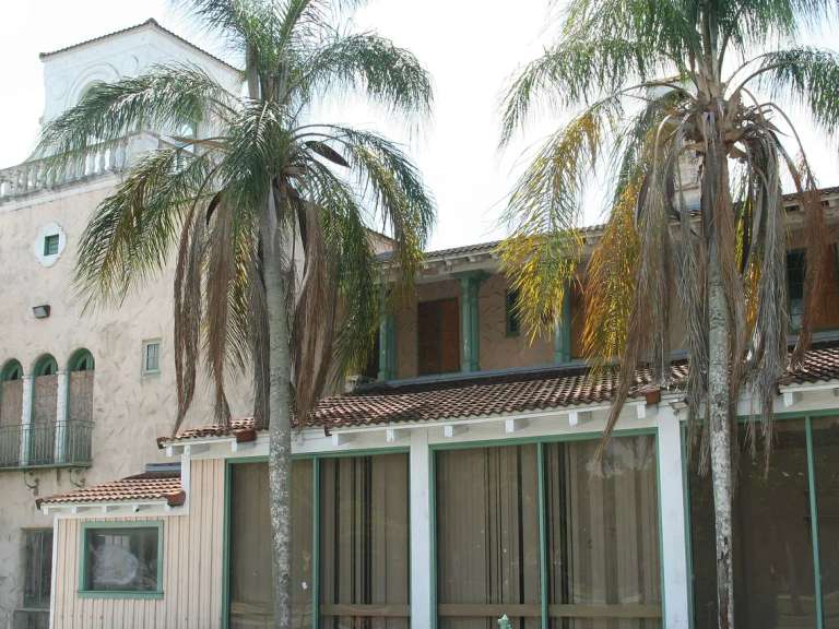 El Hacienda Hotel de New Port Richey: paredes de estuco, techo de tejas de barro y dos palmeras delante