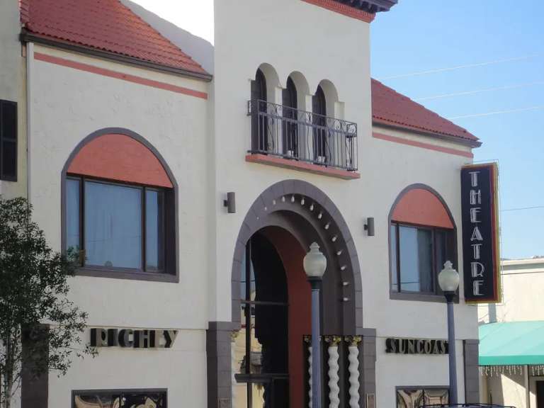 El Meighan Theatre de New Port Richey: fachada color crema con una cúpula dorada, ventanas en arco y un letrero vertical de THEATRE