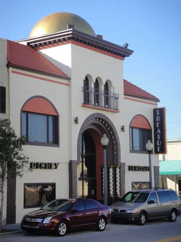 El Meighan Theatre de New Port Richey: fachada color crema con una cúpula dorada, ventanas en arco y un letrero vertical de THEATRE