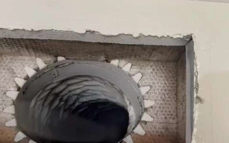 Una abertura del techo sin su rejilla, con el cuello metálico redondo y el interior oscuro del ducto de aire
